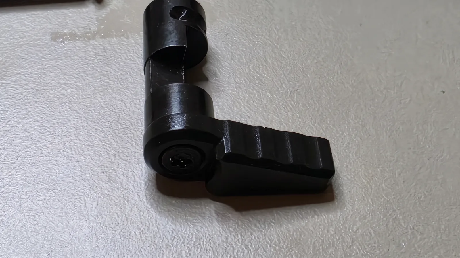 Close-up of the launch-era Partisan Disruptor safety selector, a black drum with a long serrated lever attached by a screw, lying on a bench