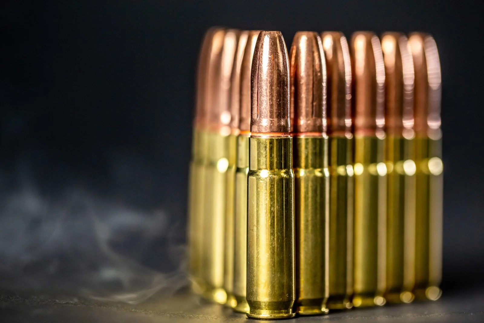 Rifle cartridges with copper bullets standing upright in low light with smoke in the background