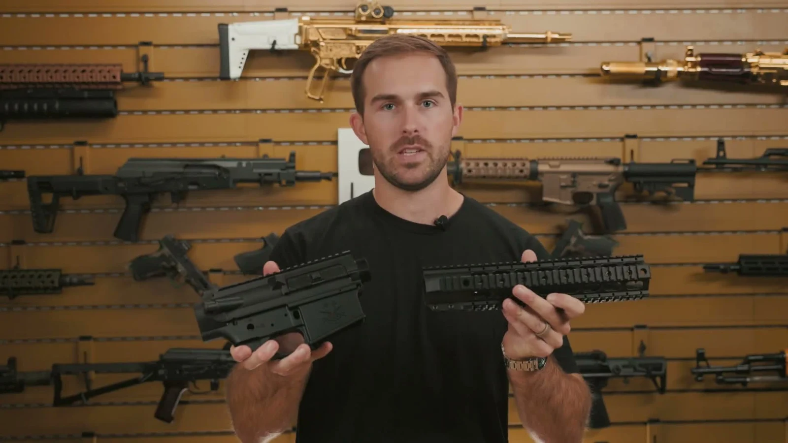 PSA presenter holding a black Sabre-10 upper and lower receiver set in one hand and the matching quad rail handguard in the other
