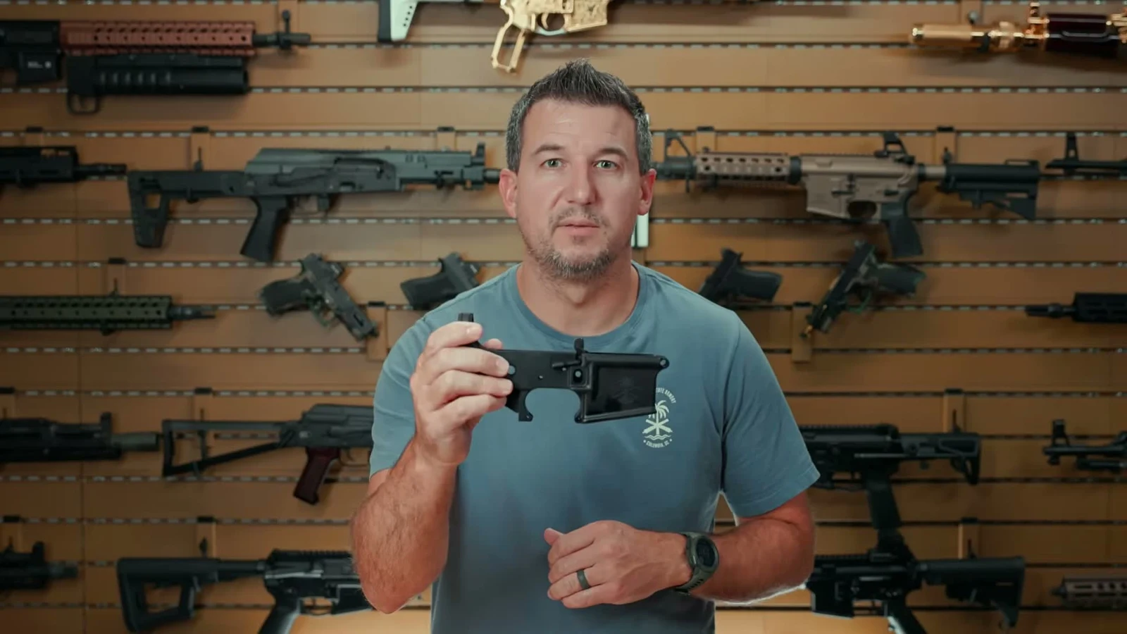 PSA presenter holding a black anodized Sabre Ambi Mil-Spec lower receiver, showing the standard mil-spec magwell profile and buffer tower
