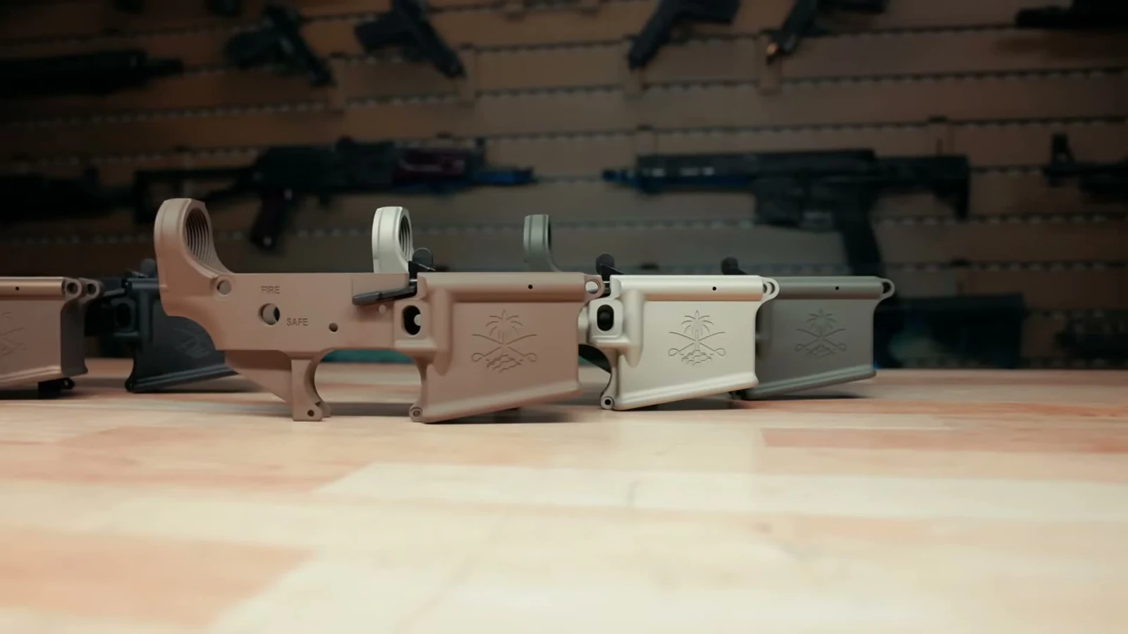 Flat Dark Earth, Champagne, and Moss Green PSA Sabre Ambi Mil-Spec lower receivers lined up on a bench, showing FIRE and SAFE markings and the ambi bolt catch paddles