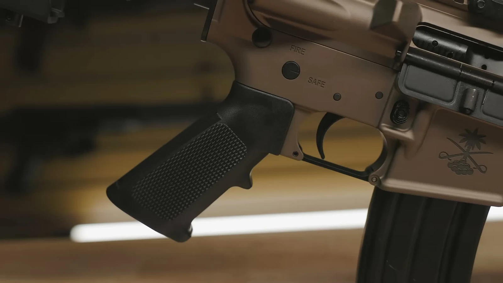 Close-up of the tan anodized Sabre M4A1 lower receiver showing FIRE and SAFE selector markings, the black A2 pistol grip, and the PSA palmetto crest