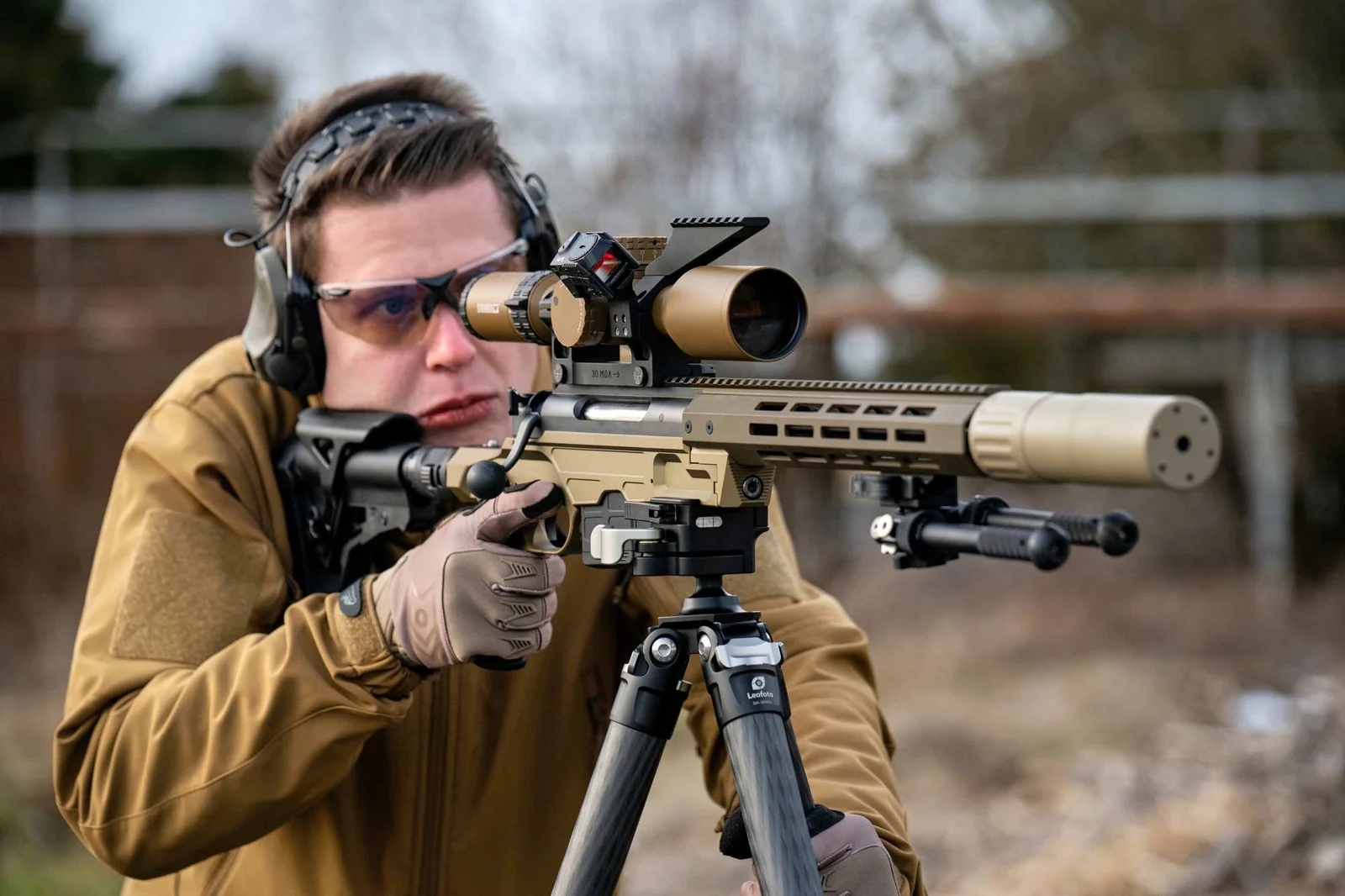Shooter prone behind a compact bolt action rifle with suppressor and bipod at an outdoor range