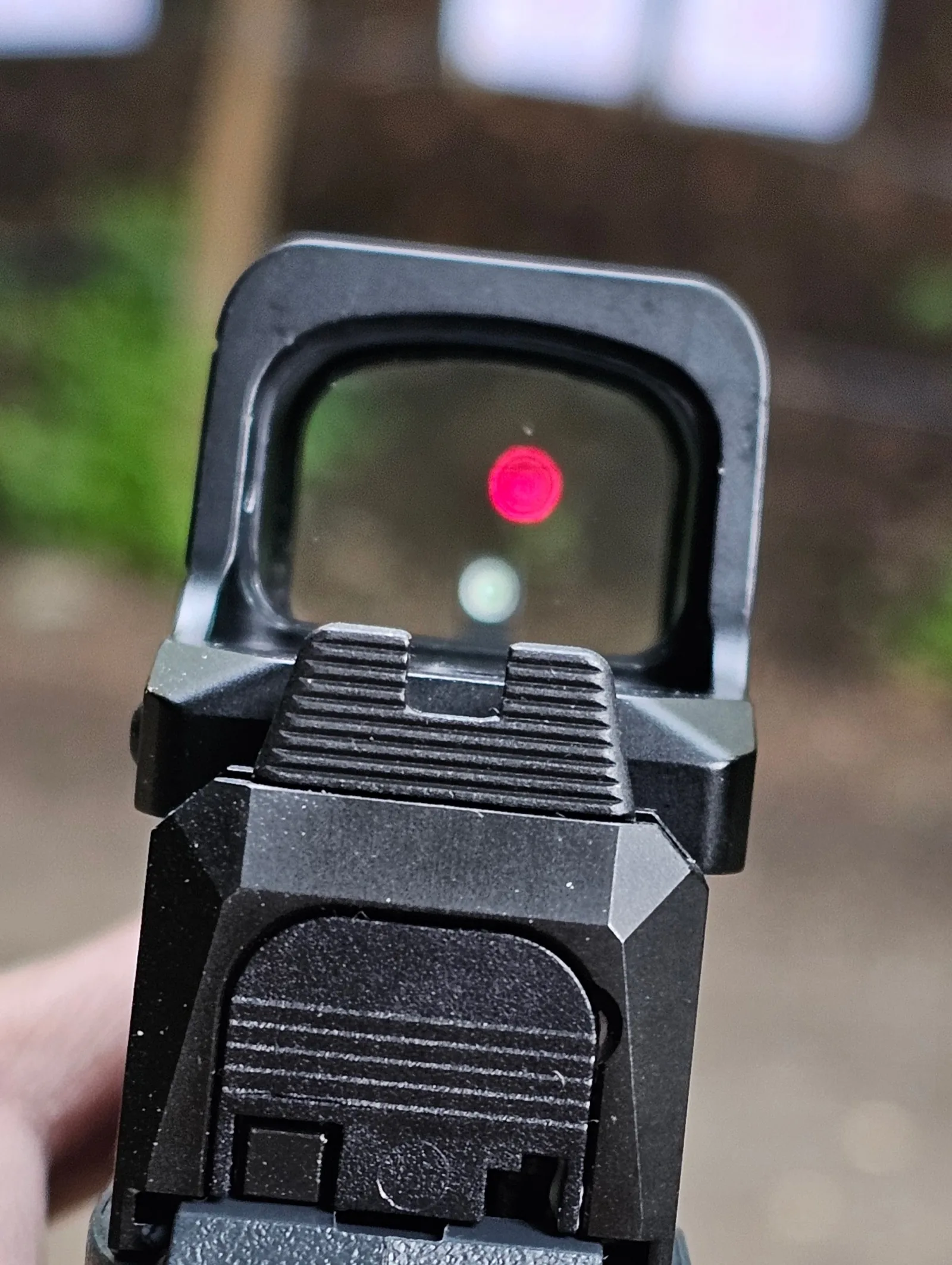 Close-up view through the back of the Ruger RXM slide showing the Osight XR red dot illuminated with the factory suppressor-height rear sight co-witnessed underneath