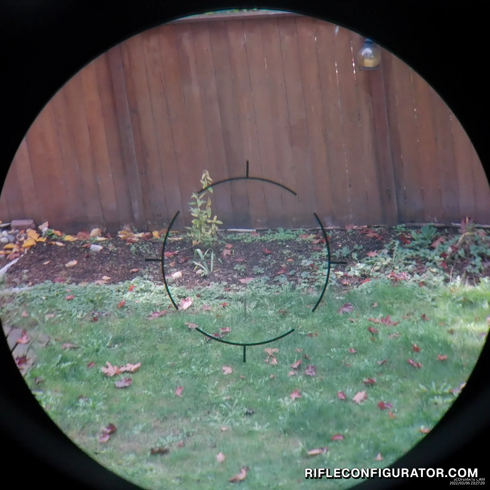 Still from a ScopeMate FFDR recording through the Vector Optics Continental at low power, the full eyepiece circle with the black rapid ring reticle on a backyard fence and lawn