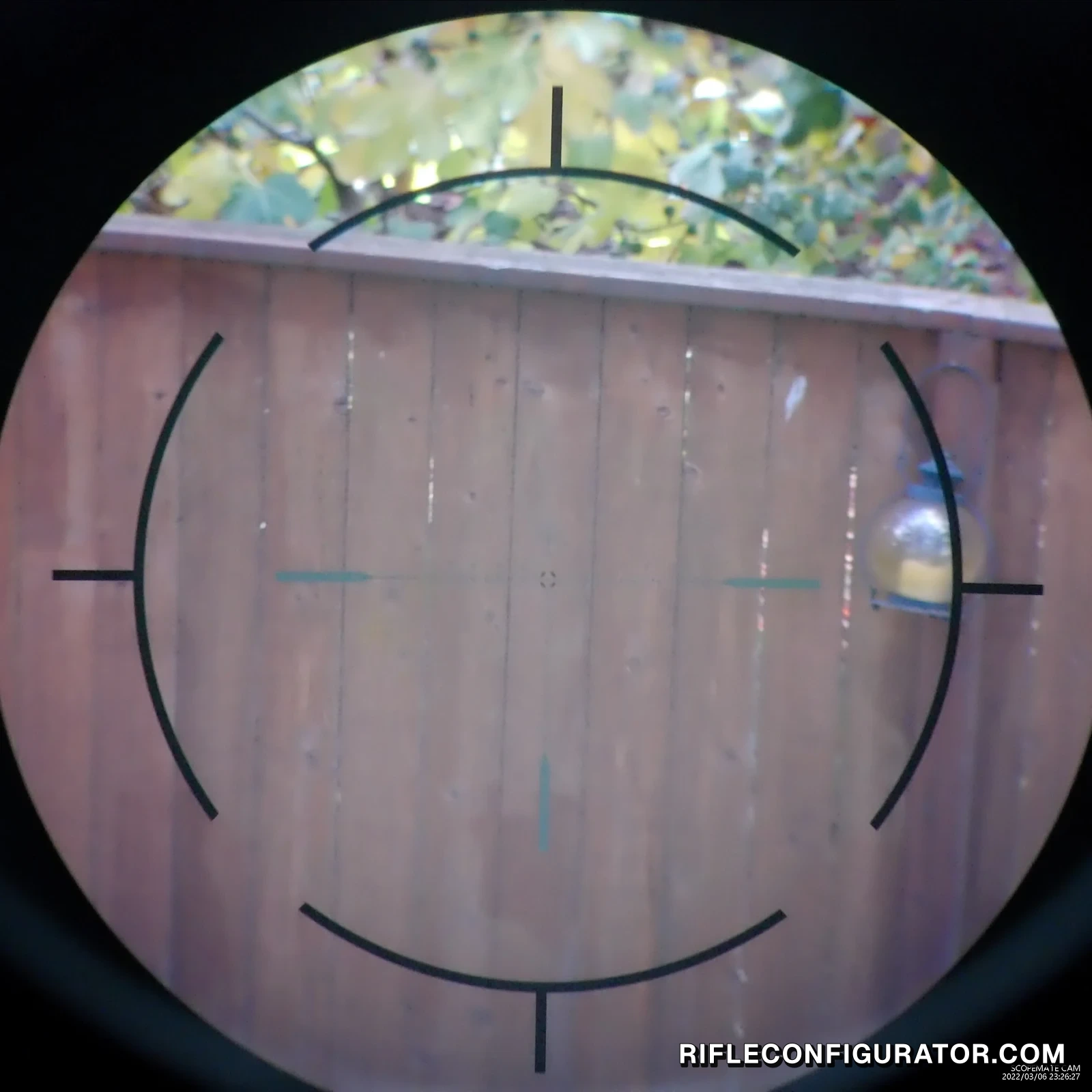 Still from a ScopeMate FFDR recording through the Vector Optics Continental at mid power, the rapid ring and crosshair on a backyard fence with trees above