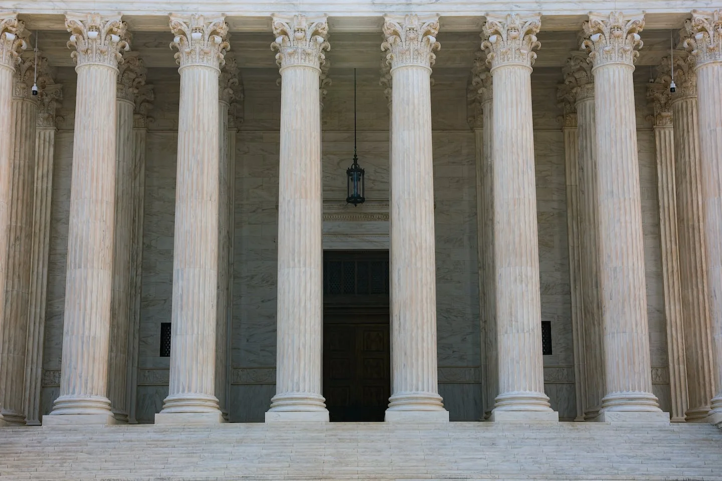 The exterior of the United States Supreme Court building in Washington D.C., with white marble columns and stone steps.