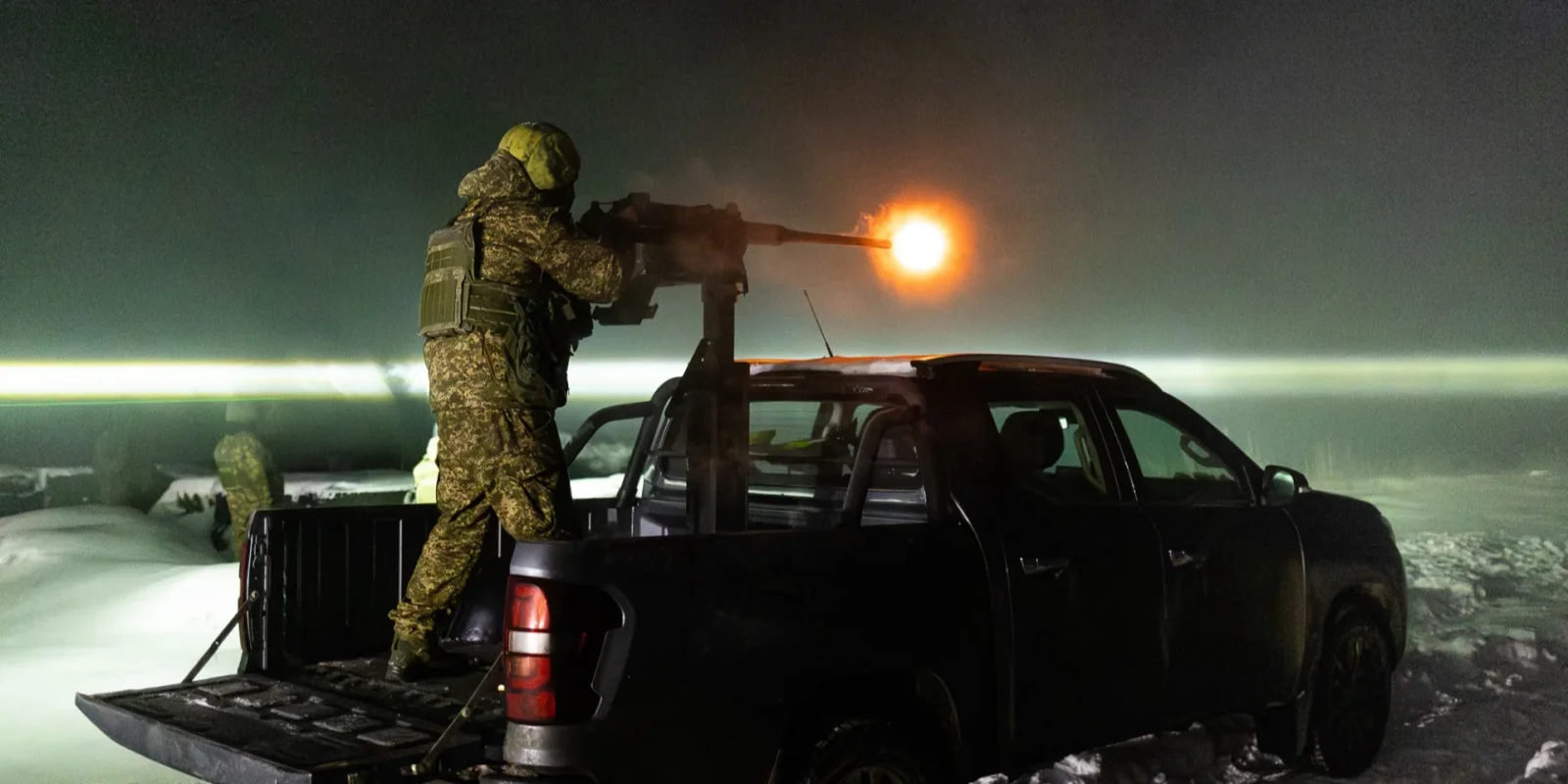 A Ukrainian soldier standing in the bed of a pickup truck at night firing a pintle-mounted heavy machine gun, muzzle flash lighting the snow-covered field