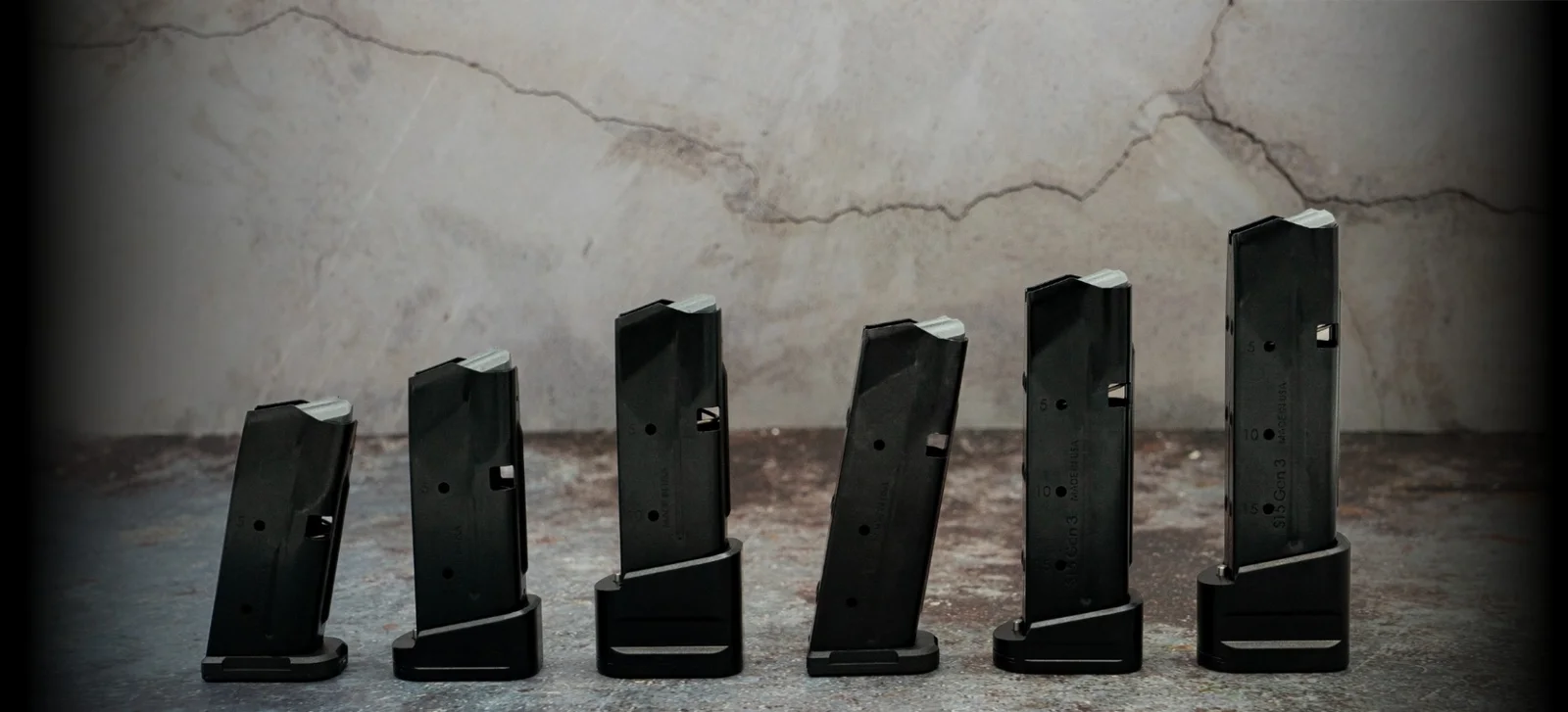 Six Shield Arms S-Series steel magazines of increasing length lined up against a concrete wall