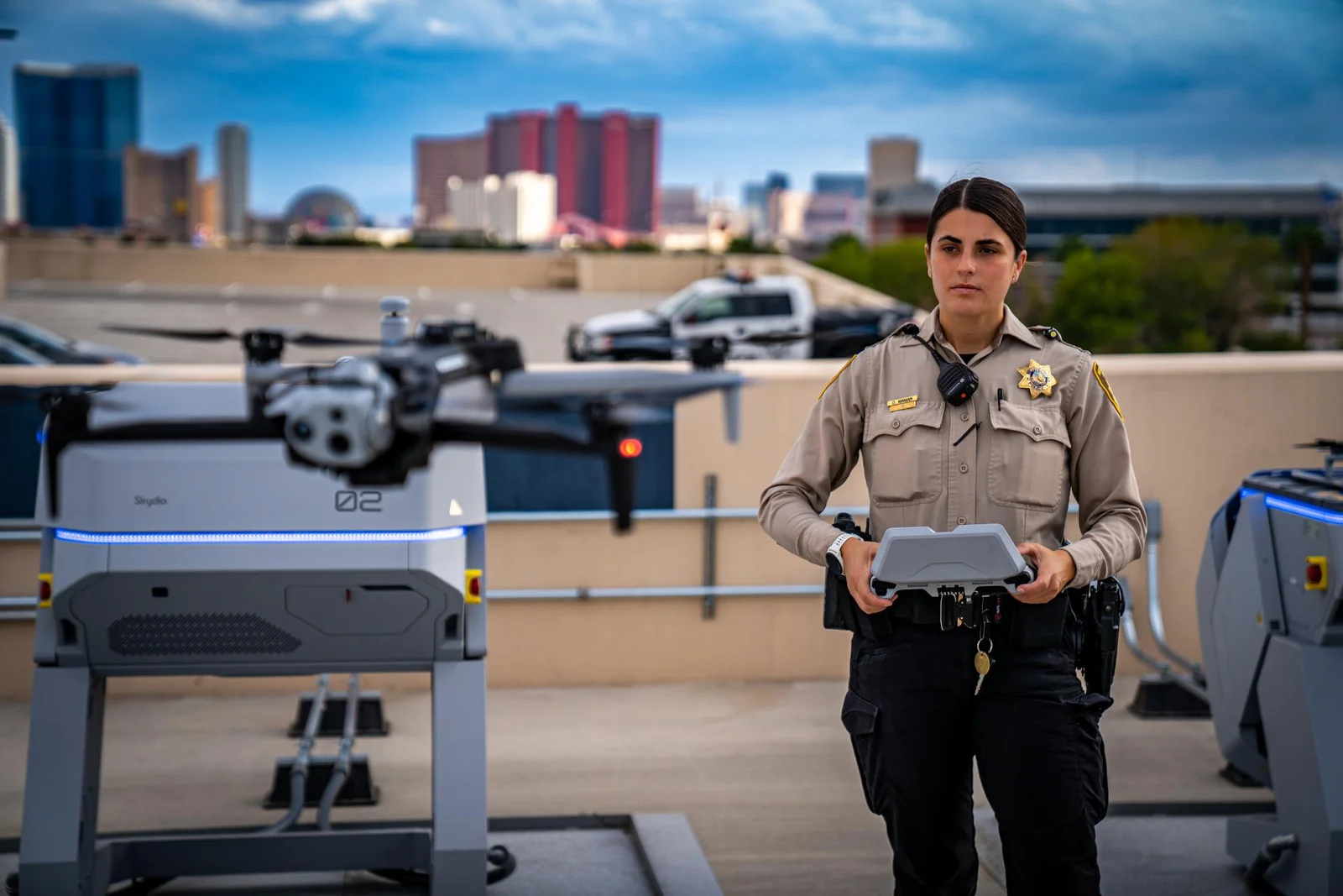 Las Vegas Metropolitan Police Department officer holding a drone controller on a rooftop beside two automated drone docking stations, with a drone lifting off in the background