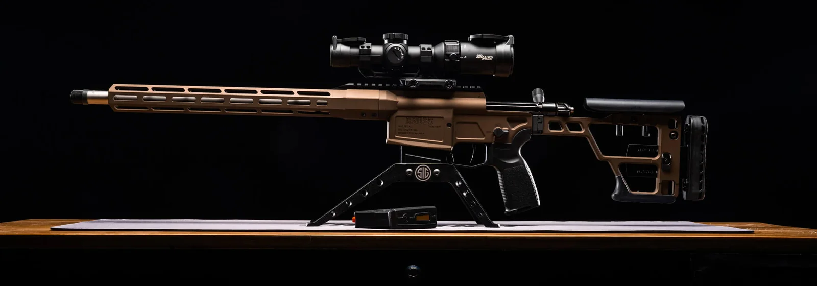 SIG Sauer Cross Bronze precision rifle in Bronze Cerakote with a scope mounted, side profile on a black studio background
