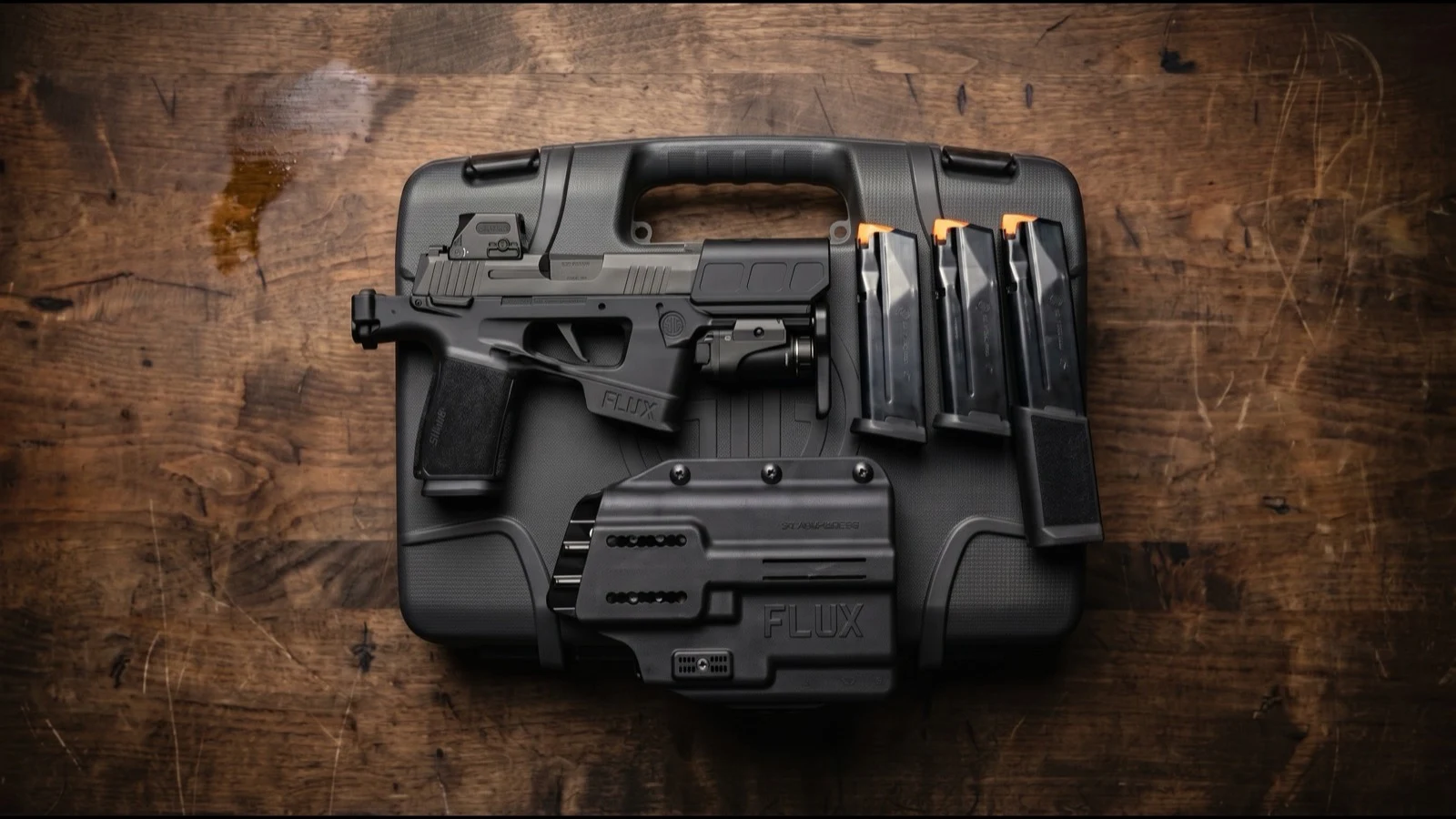 Flat-lay of the complete SIG P365-FLUX TACKIT package on a dark wood workbench: pistol with brace folded, red dot optic and weapon light installed, Flux holster, magazines, and factory hard case