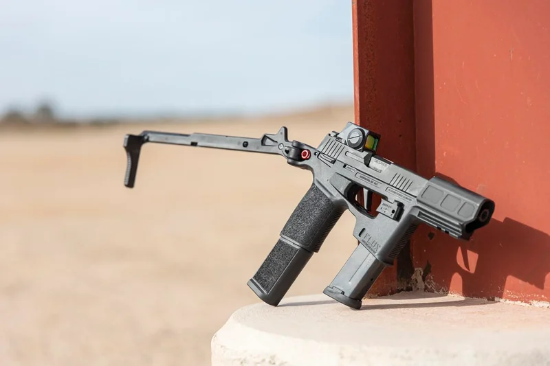 SIG P365-FLUX with brace fully deployed, propped against red metal beam at an outdoor shooting range
