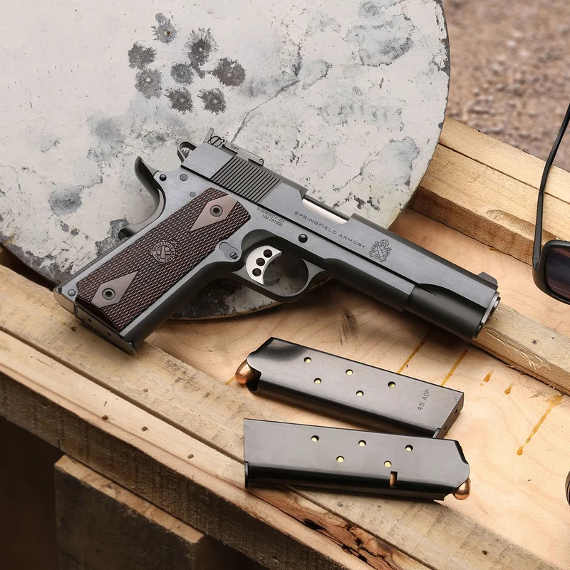 Springfield 1911 Garrison Target in hot salt blued finish on a wood bench with .45 ACP magazines and a shot-up steel target