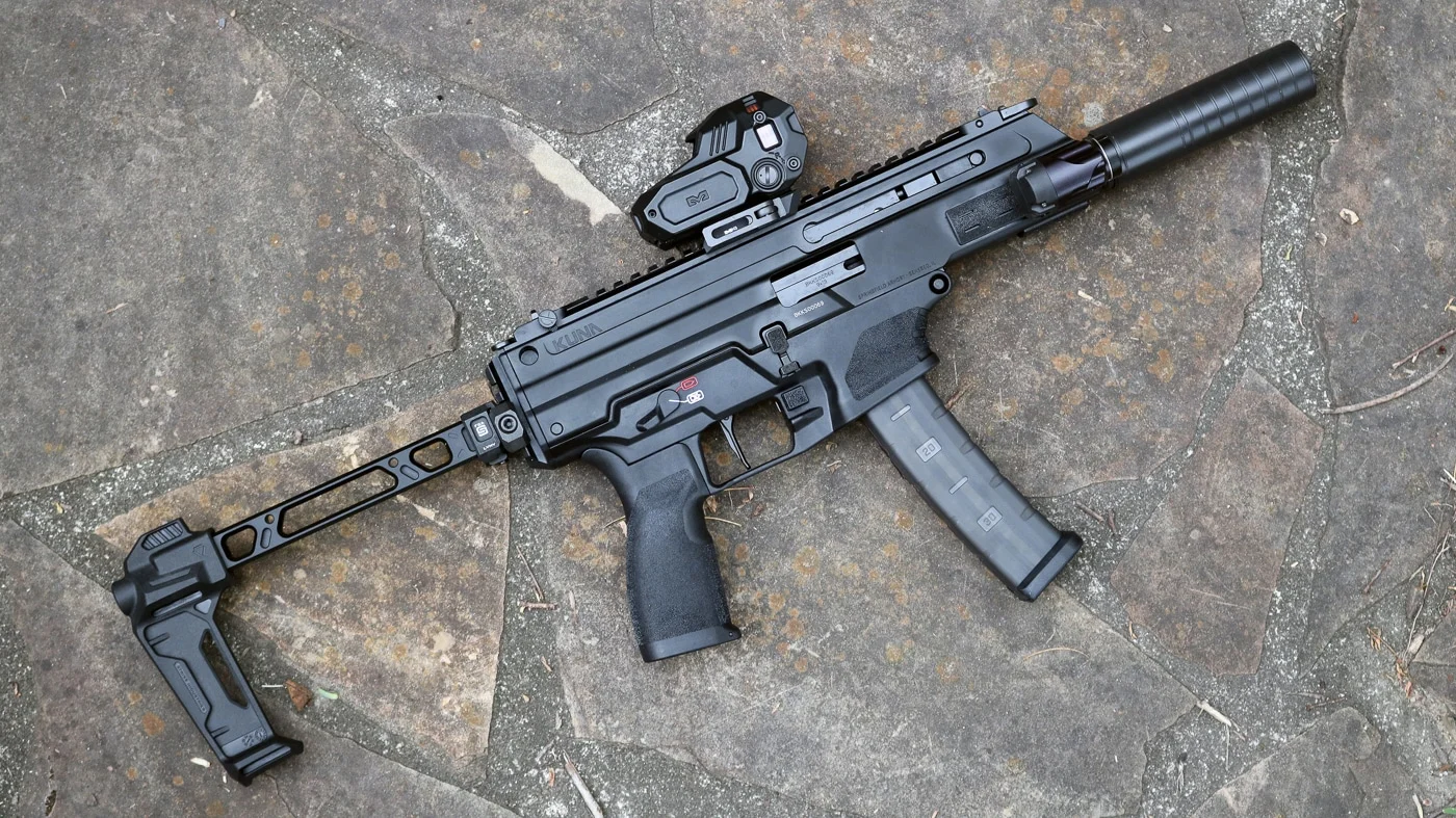 Springfield Armory Kuna 9mm laid on stone with a suppressor mounted at the muzzle, a micro red dot on the top rail, and the folding brace folded to the side