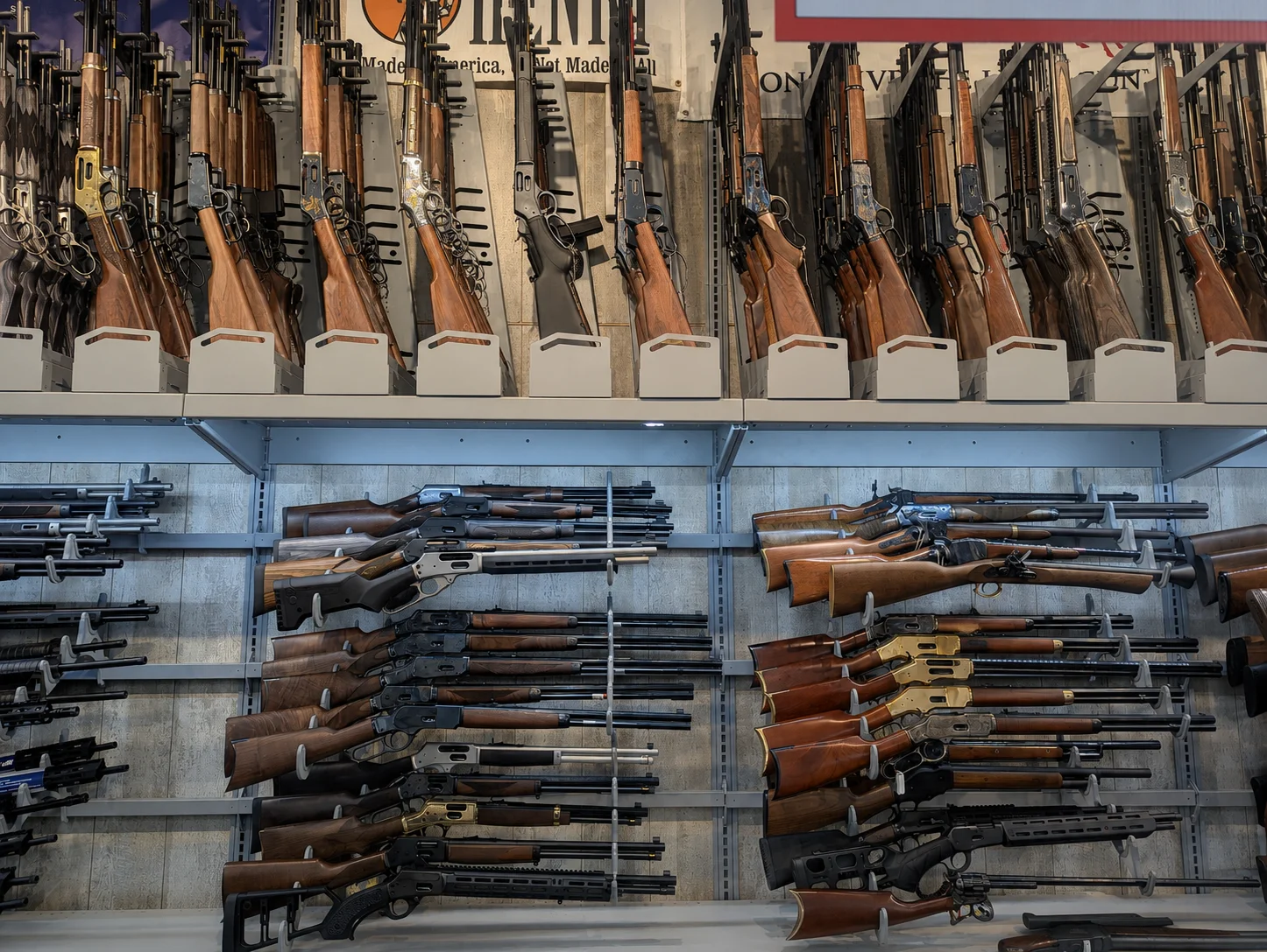 Gun store wall racked with dozens of lever-action rifles, wood and synthetic stocks, on two levels of display shelving