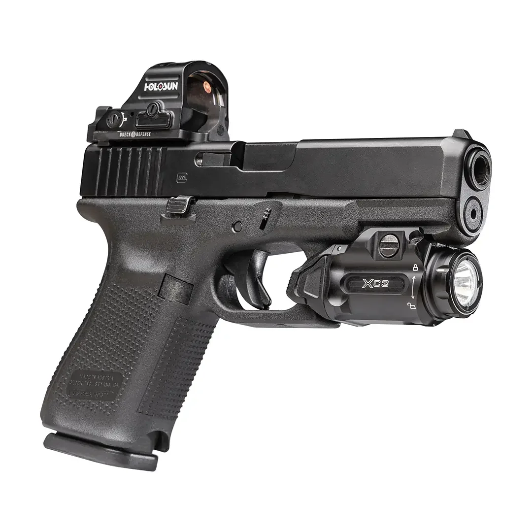 Right side of a SureFire XC3 weapon light mounted under the dust cover of a black Glock pistol fitted with a Holosun red dot, showing the XC3 marking and the lockout arrows above the clamp screw