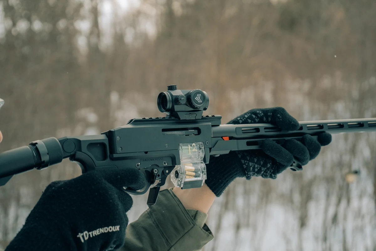 Left side of the TANDEMKROSS ADX receiver showing the charging handle slot, integral Picatinny rail with a red dot, and a clear DoubleKross magazine