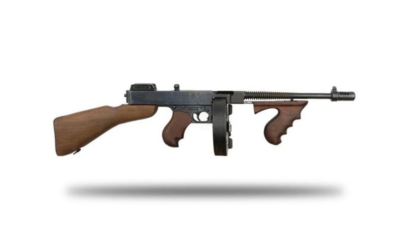 A Thompson submachine gun with a wood buttstock, vertical foregrip, drum magazine, and finned barrel with a compensator