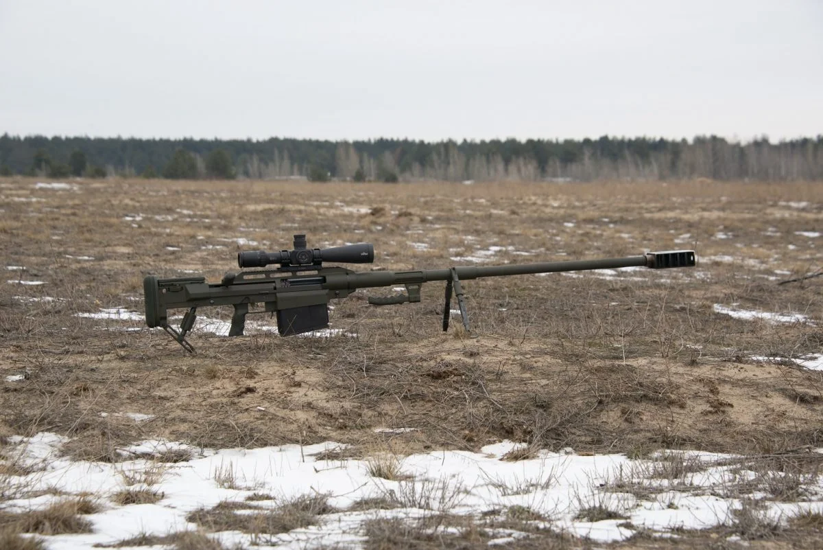 A Snipex Alligator 14.5x114mm anti-materiel rifle set up on its bipod and rear monopod on a snow-patched field with a telescopic sight fitted