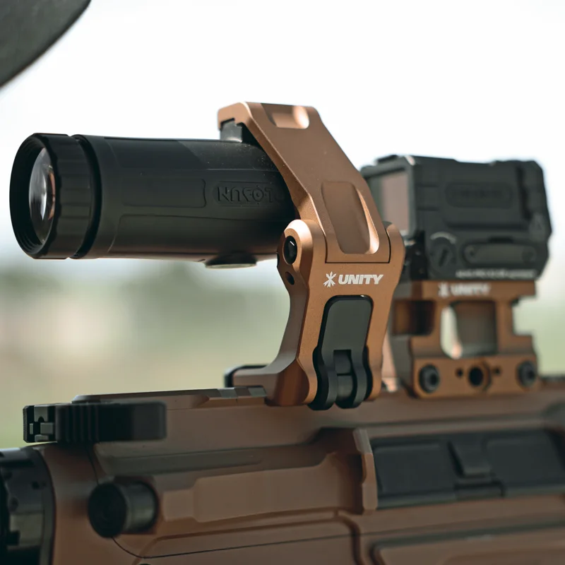 Close-up of the Unity Tactical FAST FTC Holosun mount in the raised position showing the FDE 7075-T6 aluminum body, integrated FAST QD lever, and clamp geometry around the Holosun HM3X magnifier.