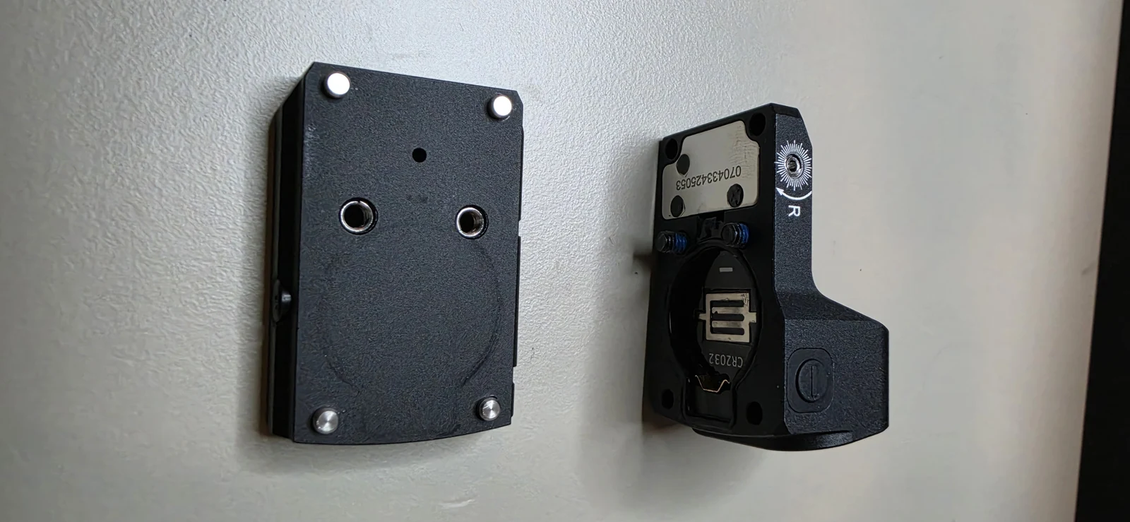 Underside of the Vector Optics Frenzy FM red dot showing the CR2032 battery tray recessed into the housing, with the separate sealing plate below it