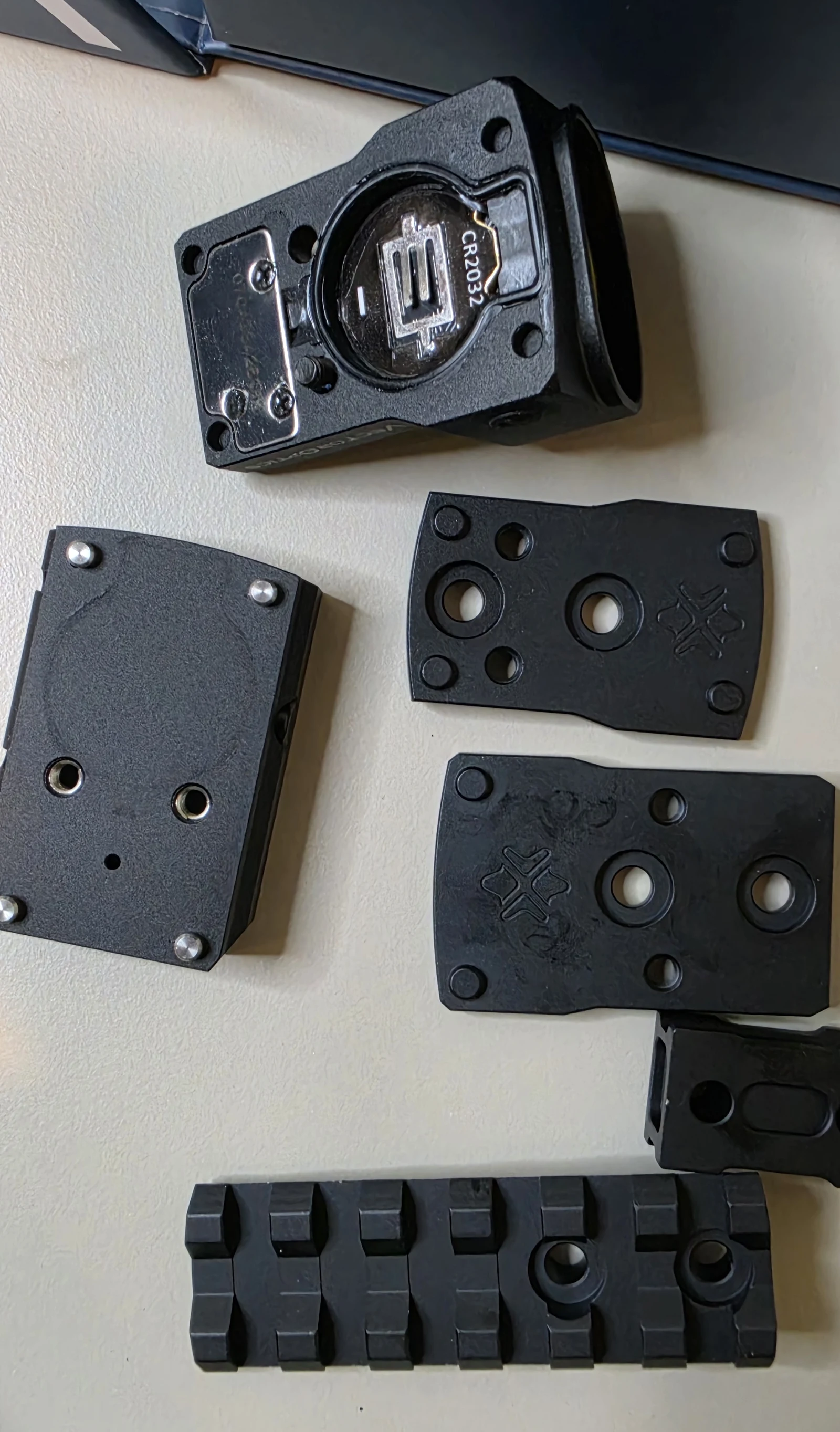 Parts of the Vector Optics X-ACCU mount assembly kit on a table: two red dot footprint adapter plates, a short Picatinny rail and a small mount piece, beside the Frenzy FM red dot and its base plate