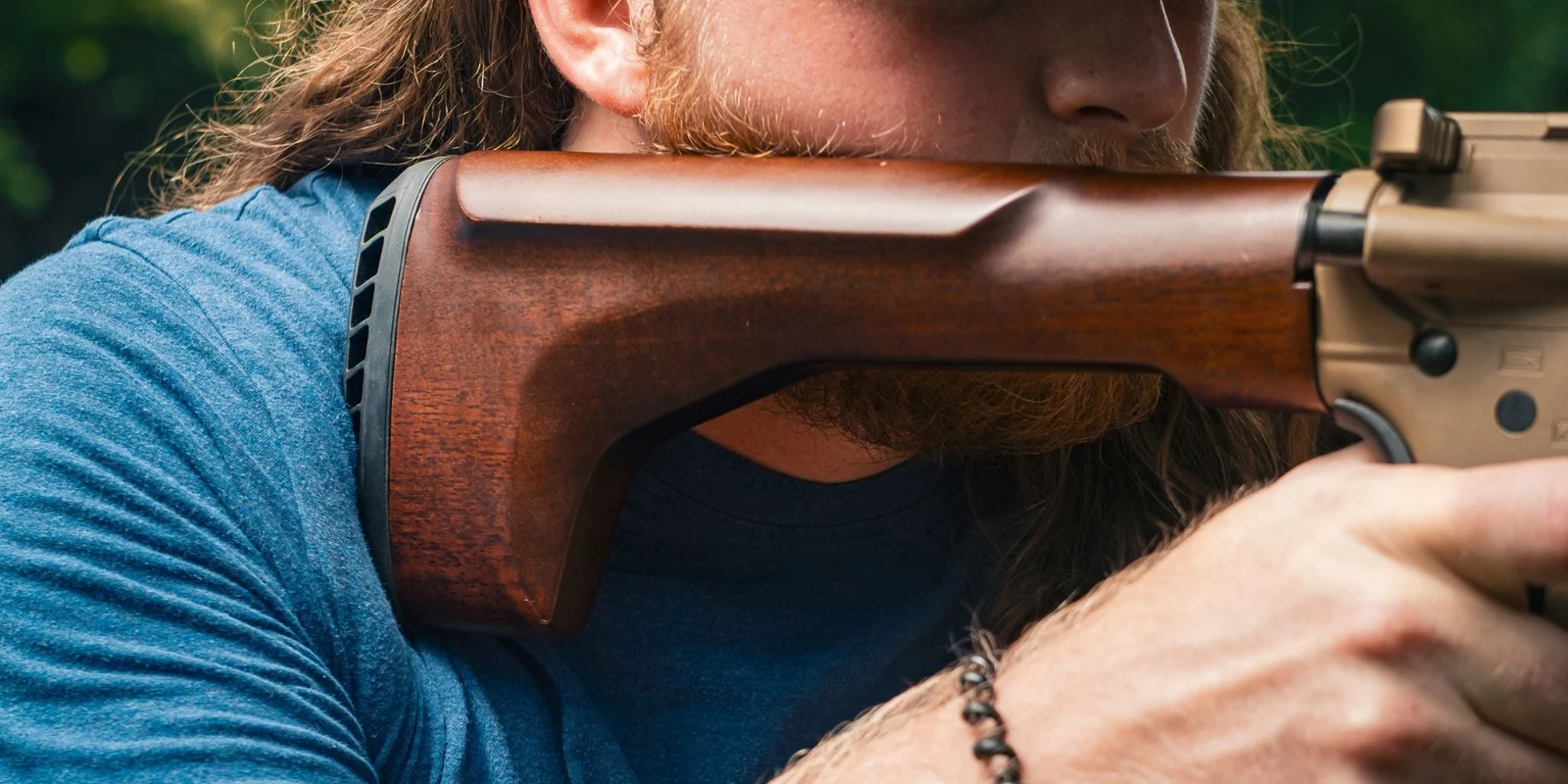 Shooter shouldering an FDE AR-15 fitted with the walnut WOOX Vigilante Fixed Stock outdoors