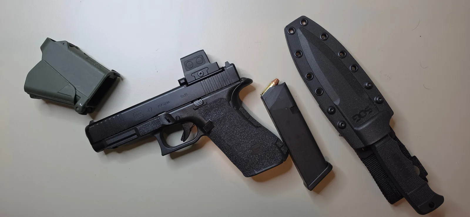 Full-size Glock with an enclosed red dot mounted directly to the factory MOS slide cut, beside a magazine, a magazine carrier, and a fixed-blade knife