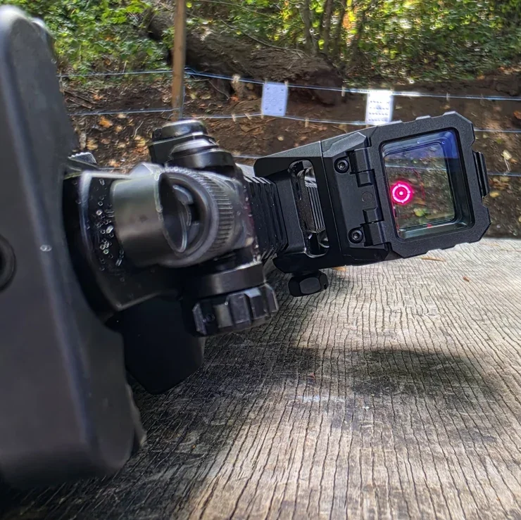 Our Holosun AEMS Pro X2 on the SR-15 at a range bench, circle-dot reticle lit in the square window with paper targets downrange