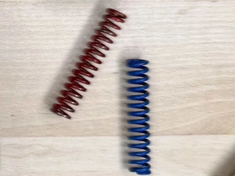 The red 17 lb and blue 19 lb Grayguns mainsprings from the Master Spring Set, out of the gun on a wood bench
