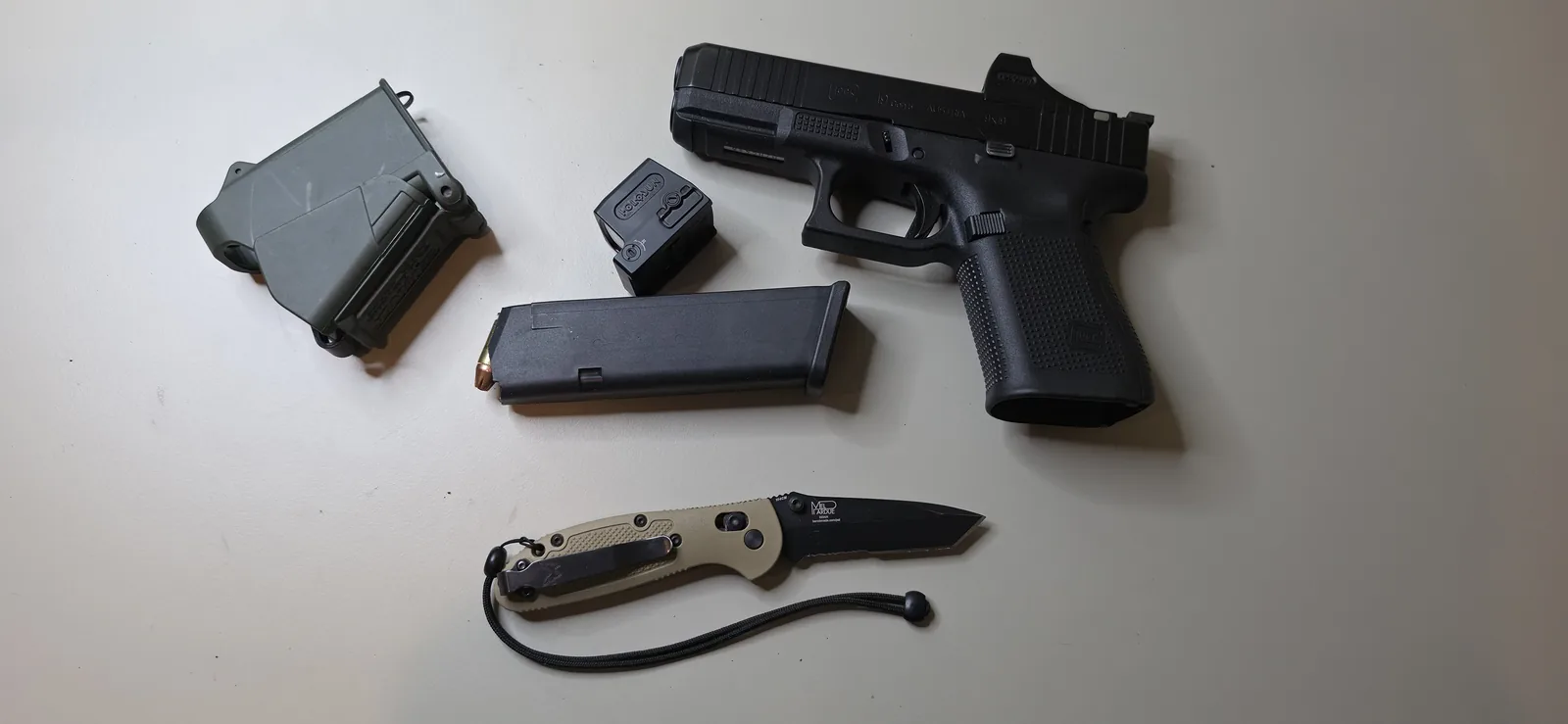 Glock 19 Gen5 MOS with a Holosun enclosed red dot mounted low in the slide cut, beside a magazine and a spare optic