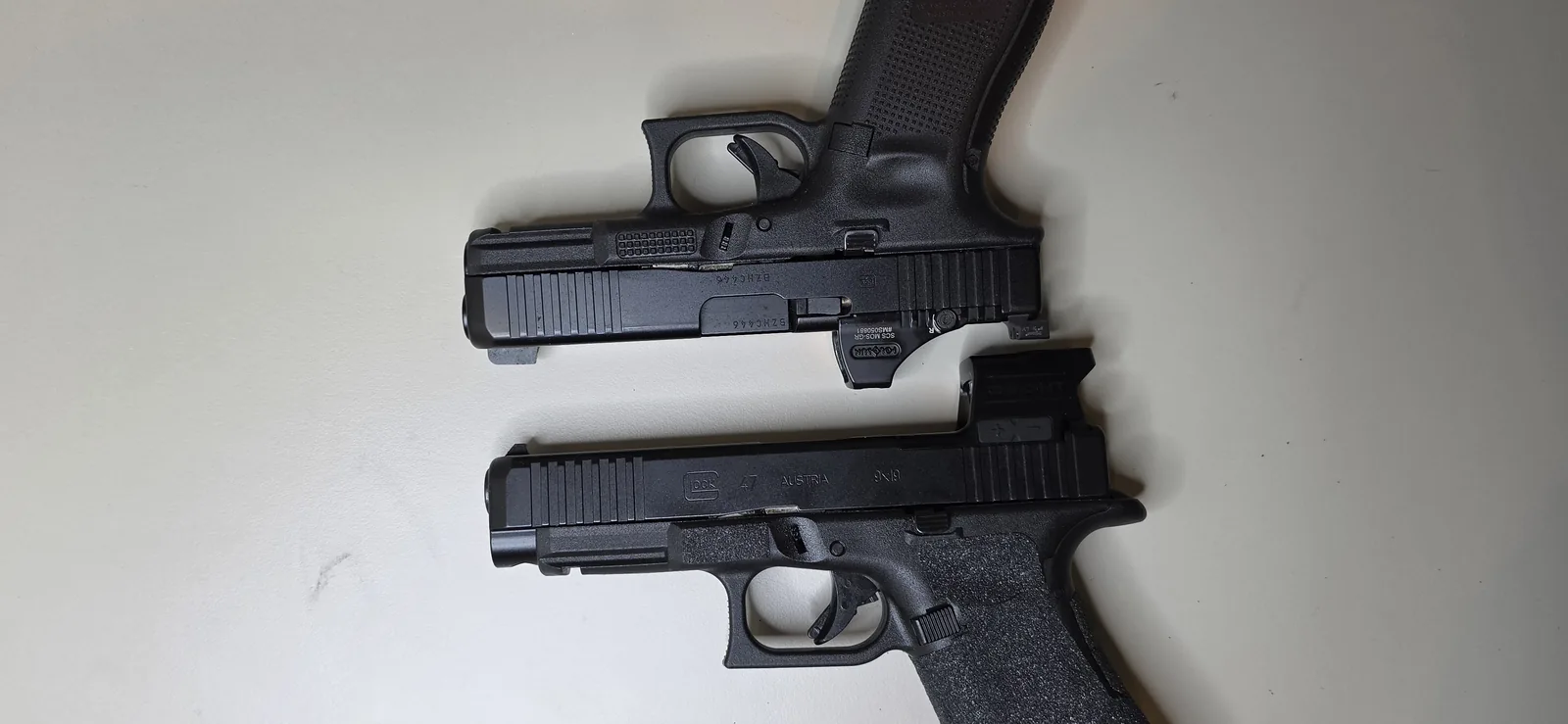 A Glock 19 Gen5 wearing a Holosun SCS MOS-GR above a full-size Glock 47 with an enclosed Osight, muzzles roughly aligned so the difference in slide length is visible
