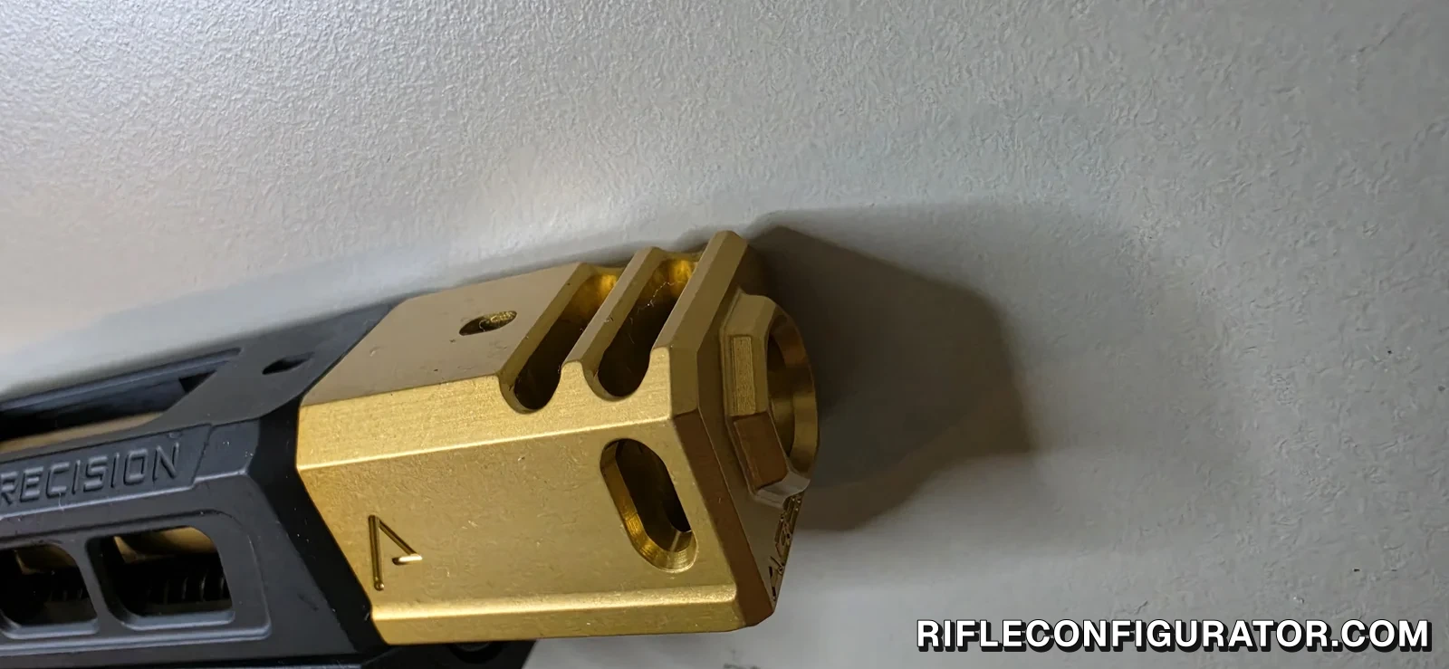 Close-up of a gold-finished pistol compensator on a black ported Glock-pattern slide, showing two vent slots across the top, a side port, and the muzzle opening at the end